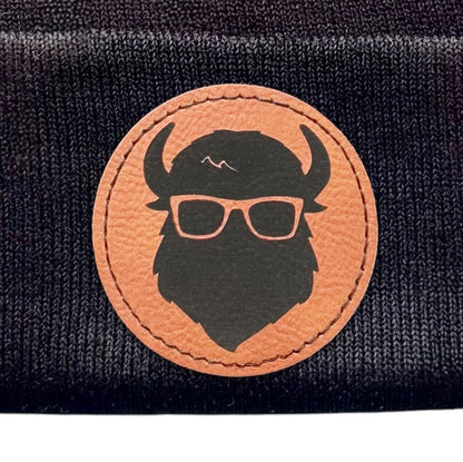 Closeup view of the leather patch on the black beanie with “The Curious Bison” logo.