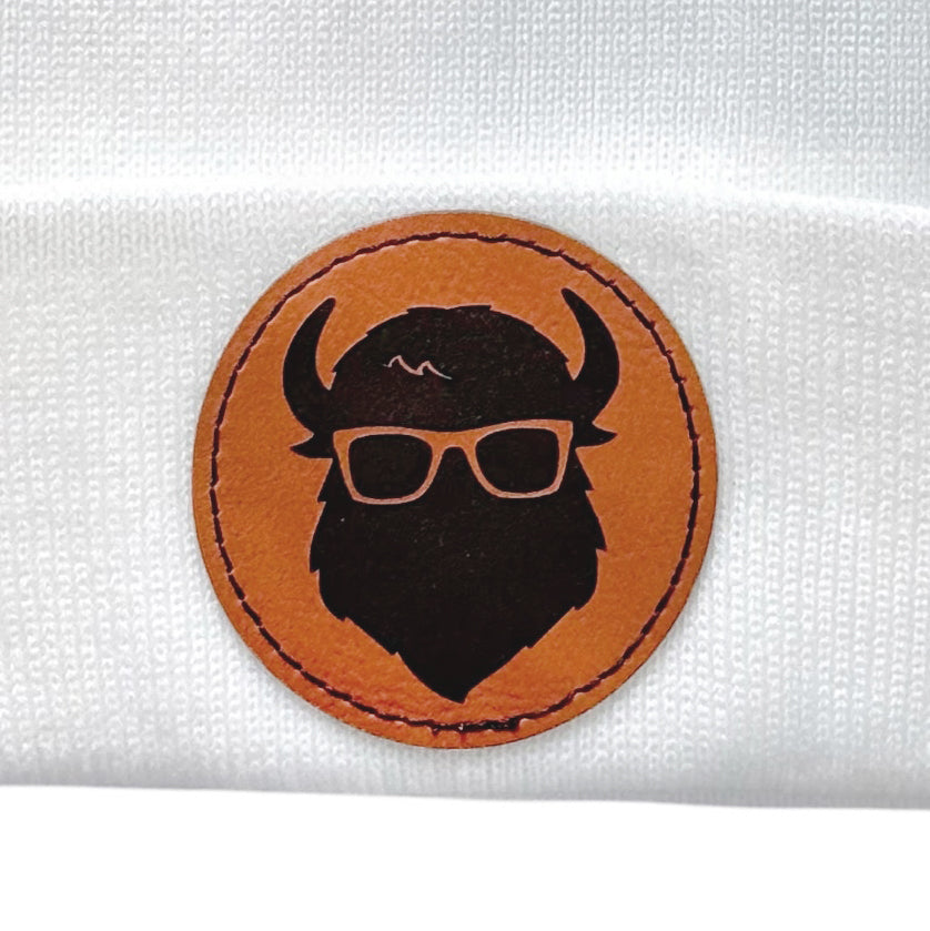 Closeup view of the leather patch on the white beanie with “The Curious Bison” logo.