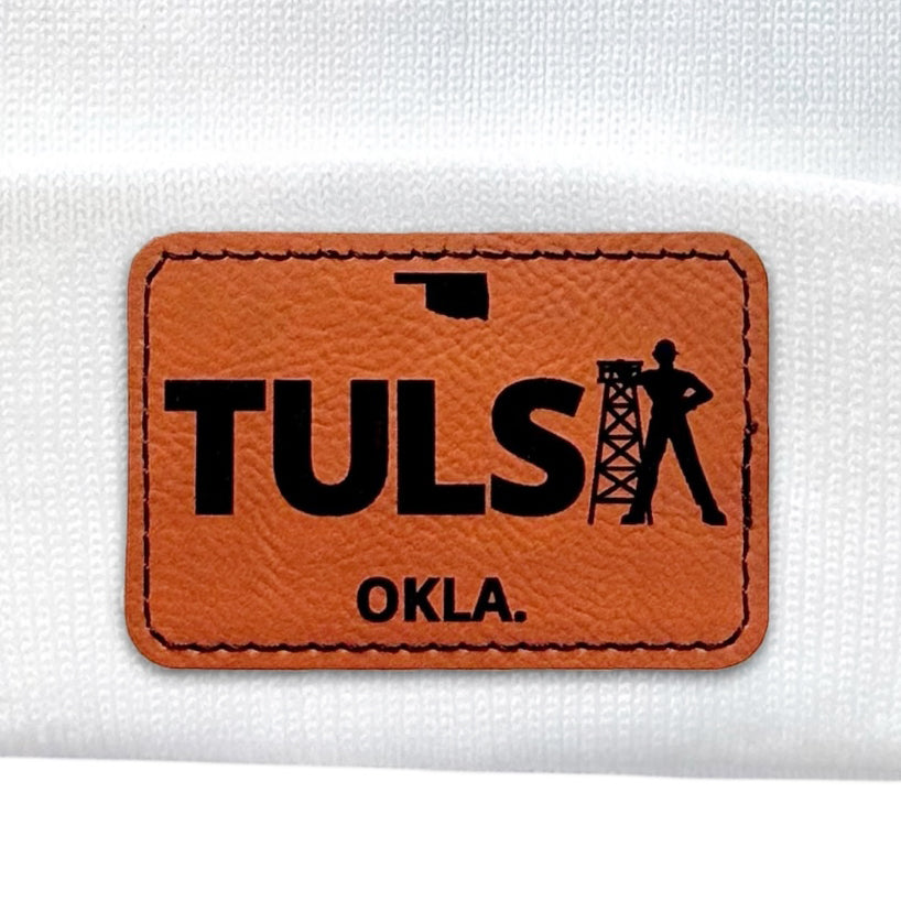 Close-up of a white knit beanie highlighting the leather Tulsa Driller patch with sharp detailing.