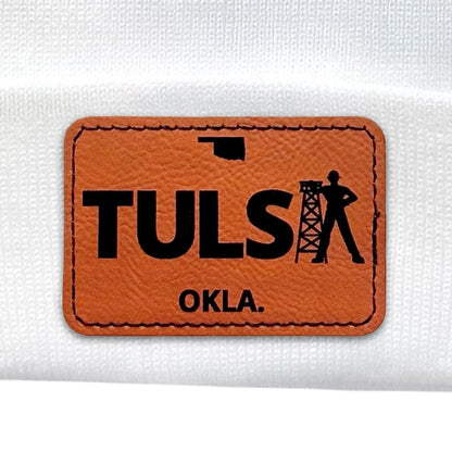 Close-up of a white knit beanie highlighting the leather Tulsa Driller patch with sharp detailing.